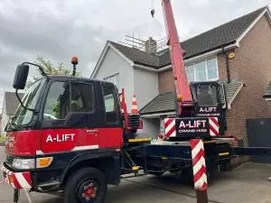 A-LIFT crane truck with raised red boom parked outside a brick house