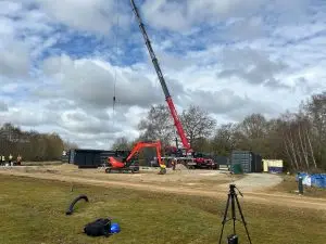 Red and black crane with raised boom at a work site under a cloudy sky