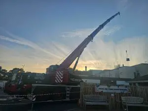 Mobile crane with extended boom lifting a small load near buildings at sunset