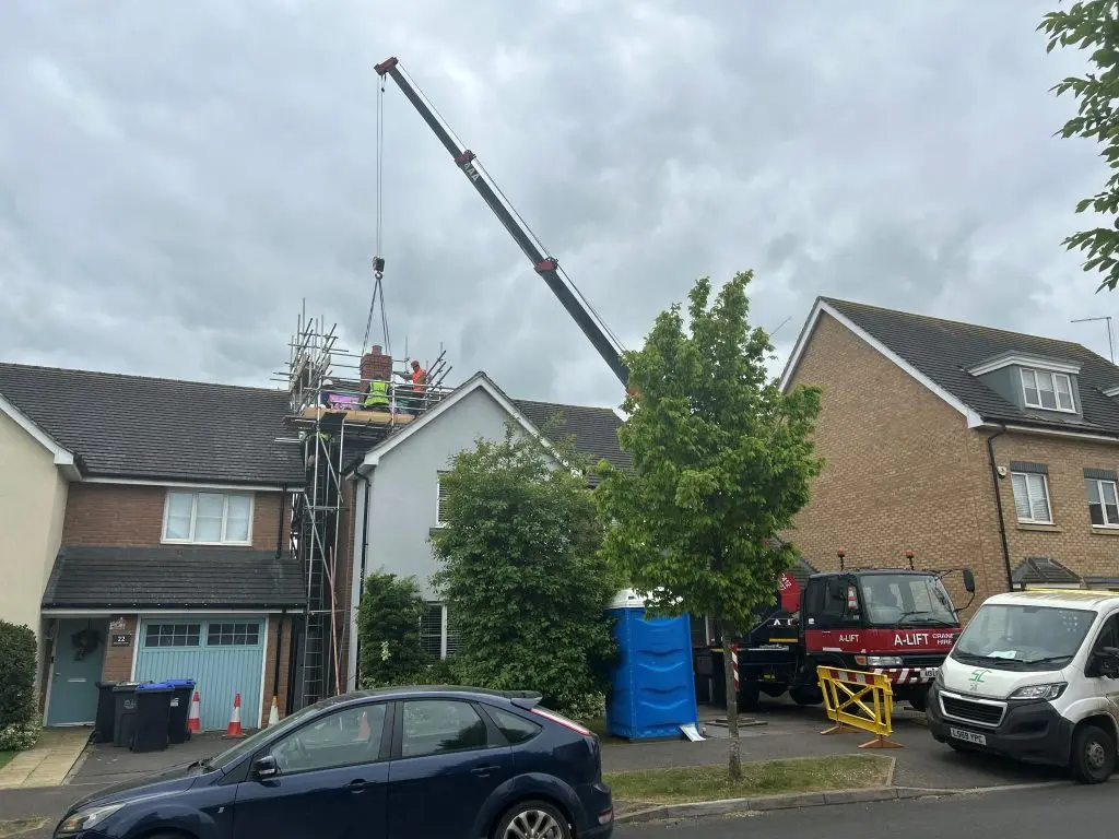 Crane lifting materials to scaffolding outside a house on a residential street