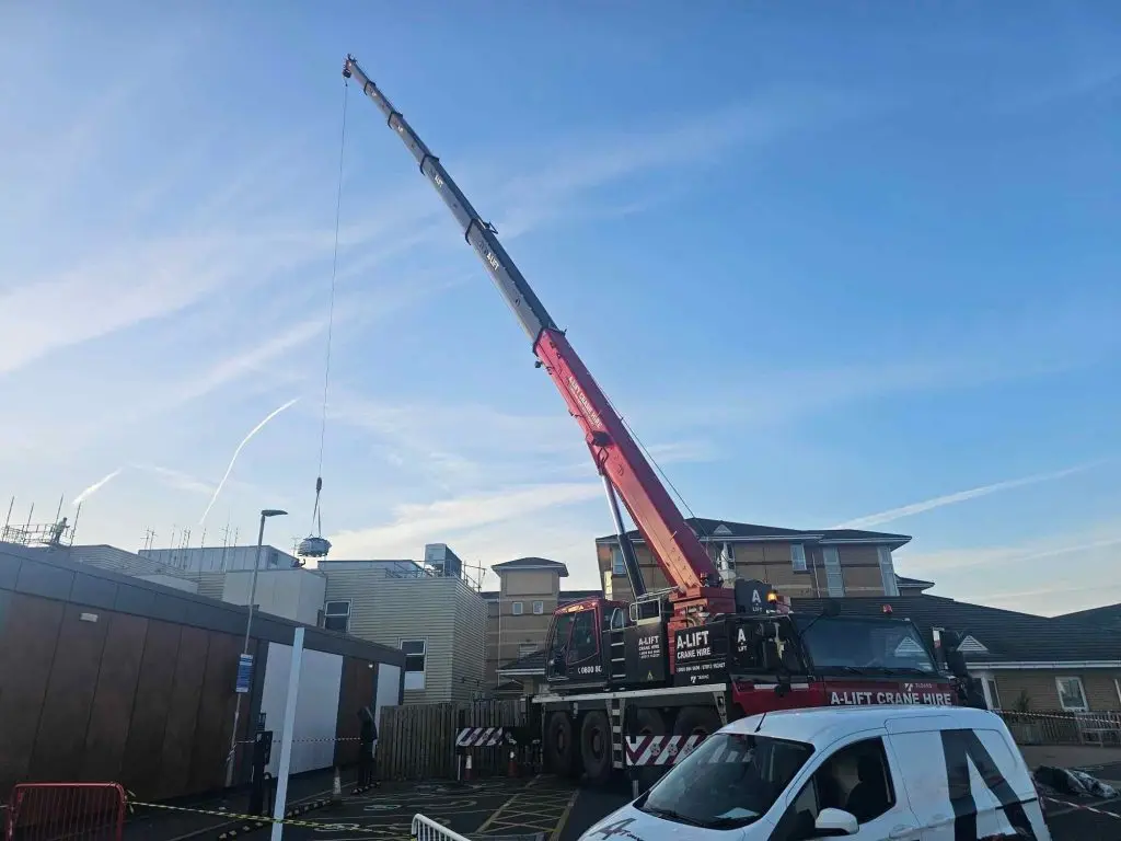 Red mobile crane lifting equipment above buildings against a blue sky