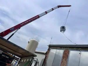 A-Lift Crane Hire crane lifting a cylindrical unit above a brick building roof