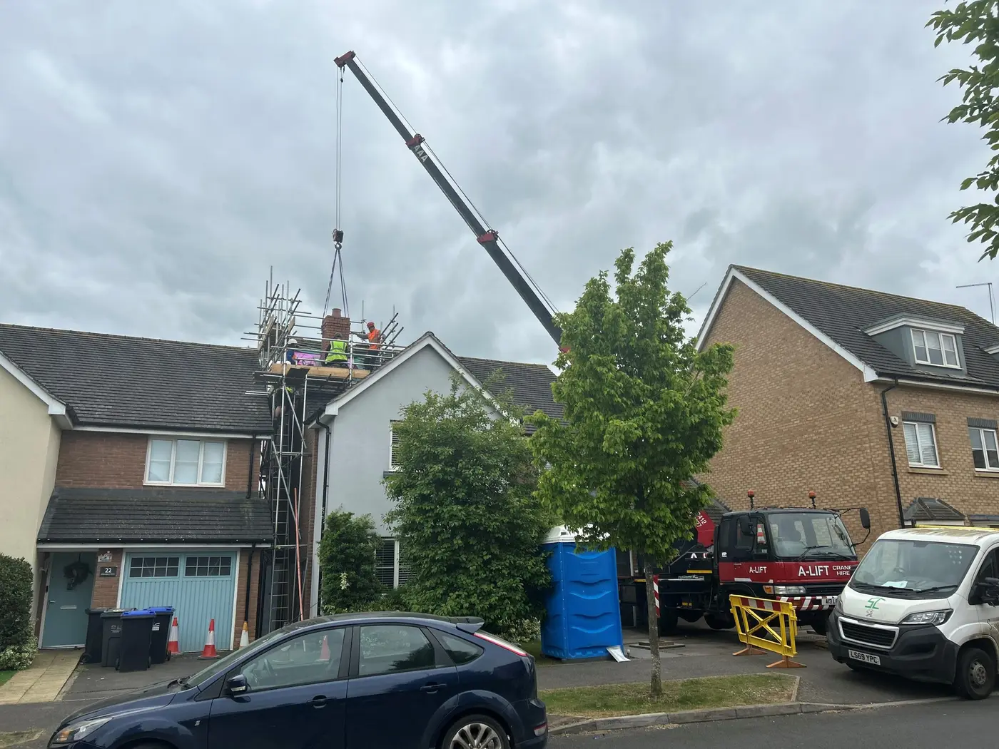 A-Lift mobile crane lifting a load to workers on rooftop scaffolding between houses