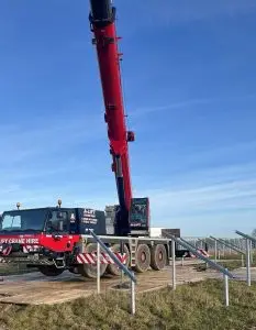 Red mobile crane truck with raised boom behind a metal railing under a blue sky