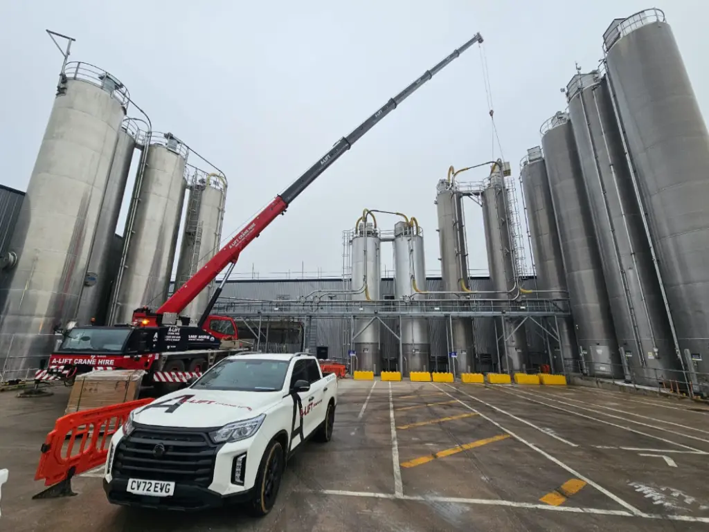 Mobile crane lifting equipment between tall industrial silos