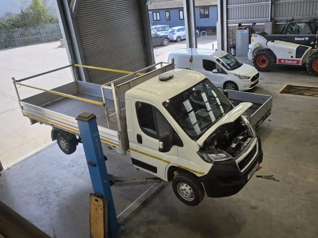 White flatbed truck raised on a workshop lift with its hood open