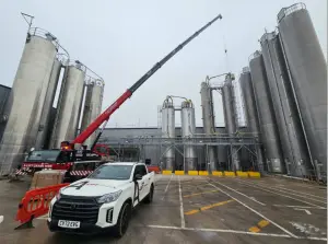 Red mobile crane and white pickup parked beside tall industrial silos