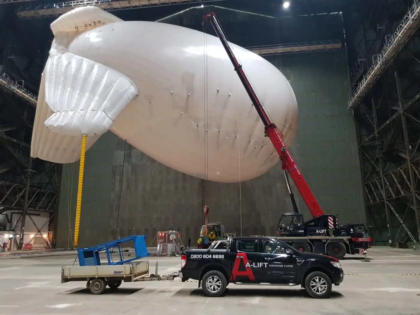 A-Lift crane and pickup beside a large white inflatable airship indoors