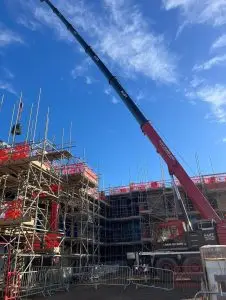 Red mobile crane with long boom beside a scaffolded building under a blue sky