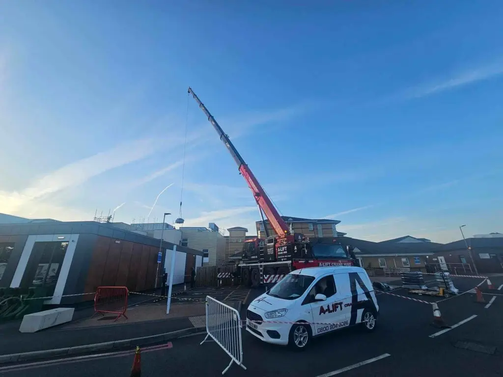 Mobile crane lifting equipment beside a branded A-Lift Crane Hire van in a paved work area