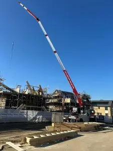 Red and white mobile crane with boom extended over a scaffolded construction site