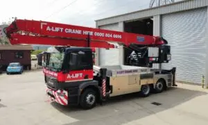 A-Lift mobile crane truck with red boom parked beside an industrial building