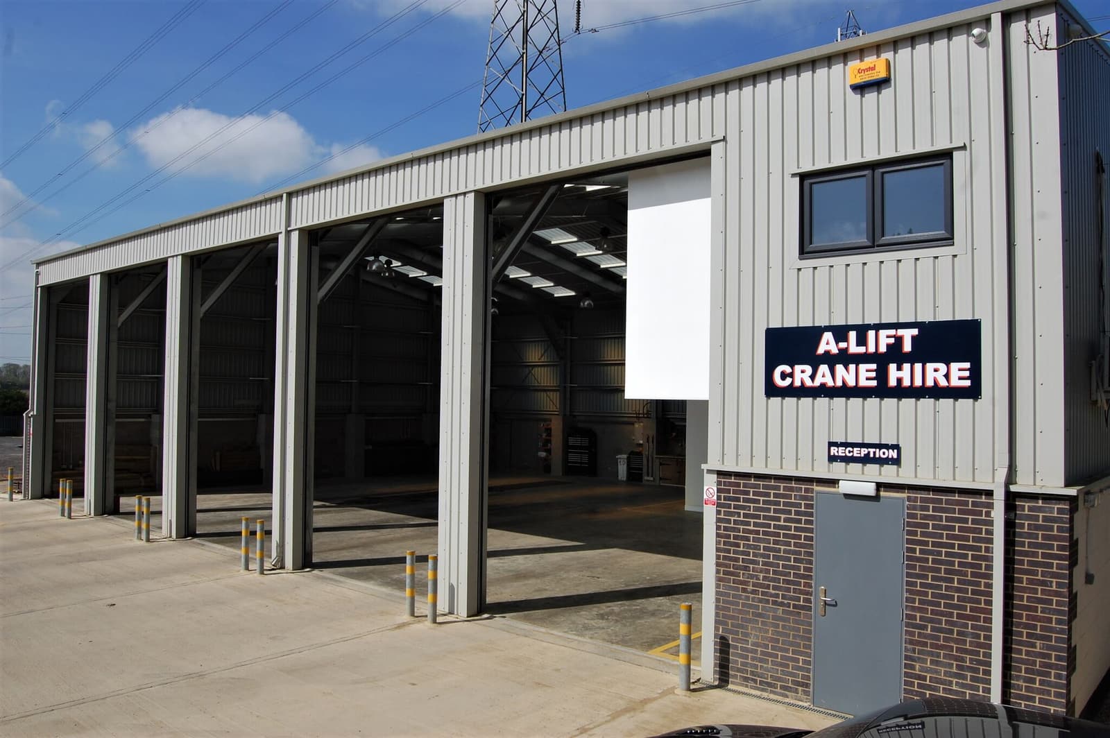 A-LIFT CRANE HIRE sign on a metal industrial building with open garage bays and reception door